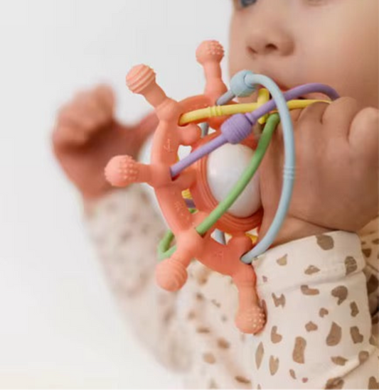 Baby chewing on the pink silicone teething toy, holding it with both hands.