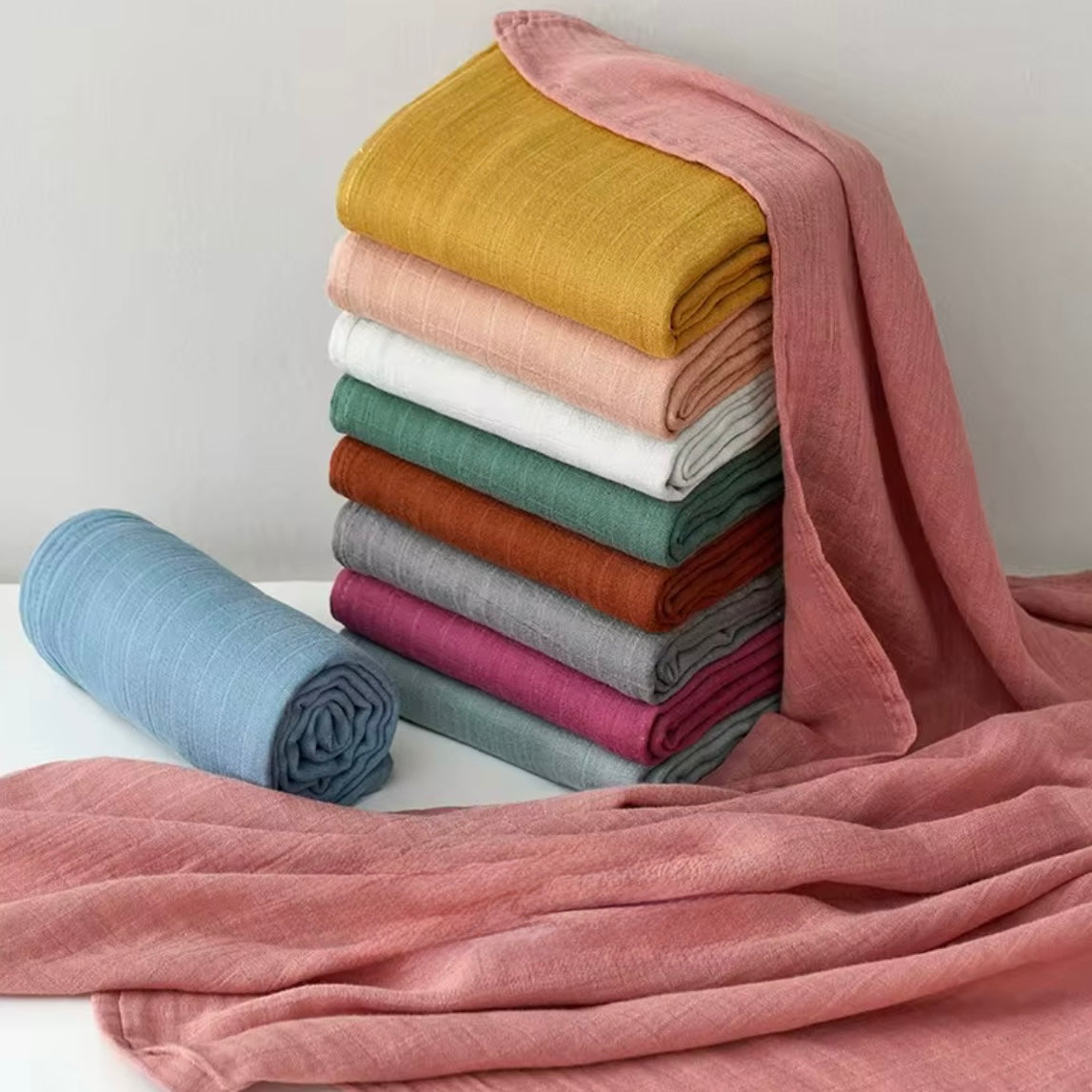 Stack of premium muslin baby wraps in neutral and pastel shades, soft and cozy.