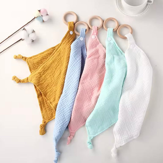 Set of five pastel muslin comforters with wooden teethers in mustard, baby blue, blush pink, mint, and white.