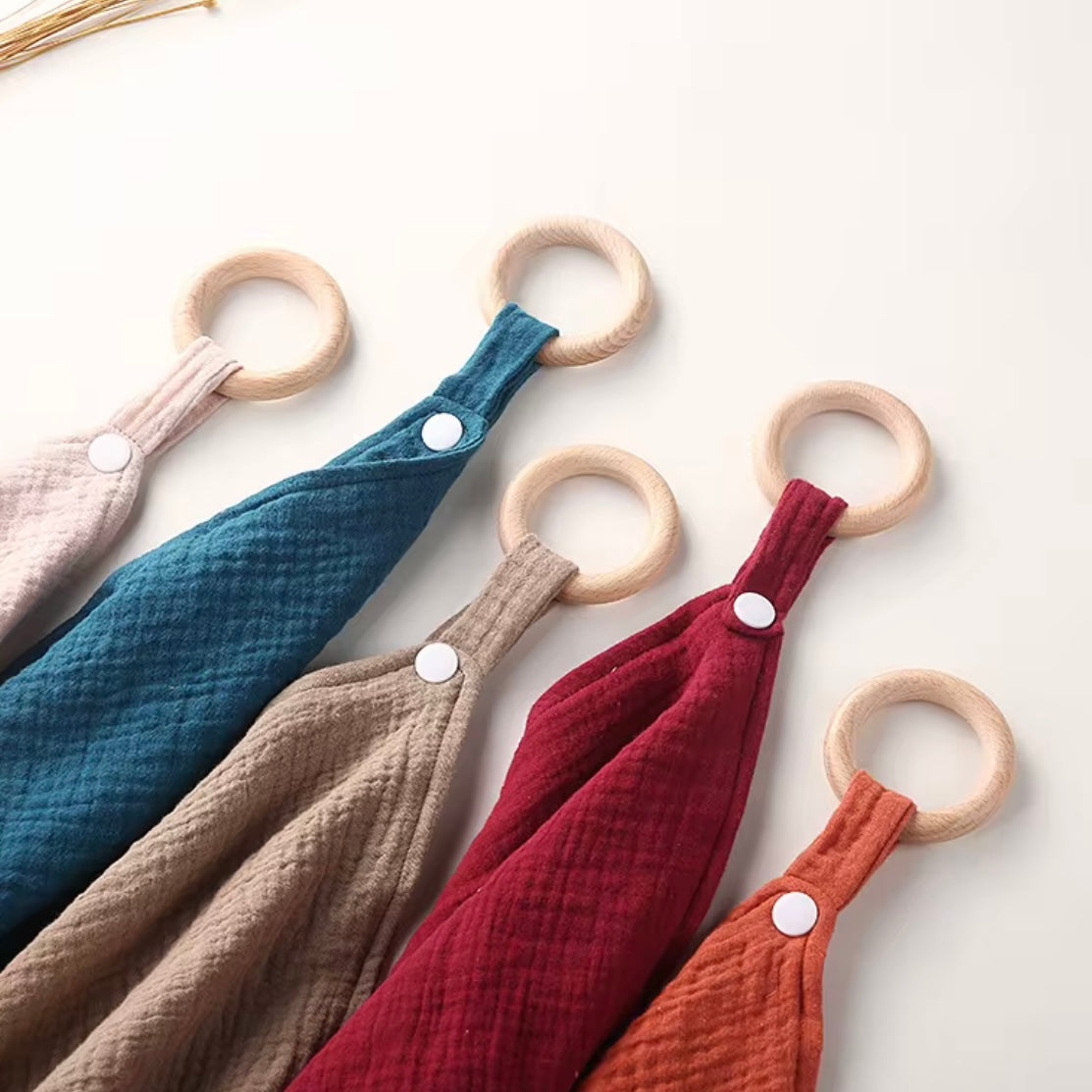 Close-up of wooden teething rings attached to soft muslin comforters in earthy colours, perfect for babies to cuddle and chew.