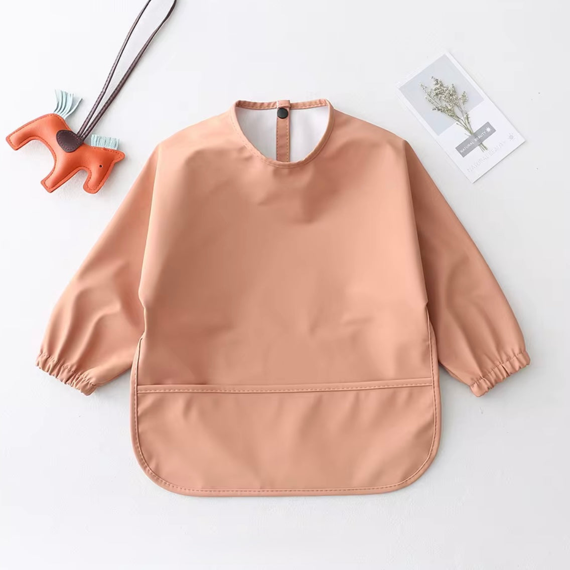 Peach-toned sleeved smock bib for babies and toddlers, waterproof and wipeable.