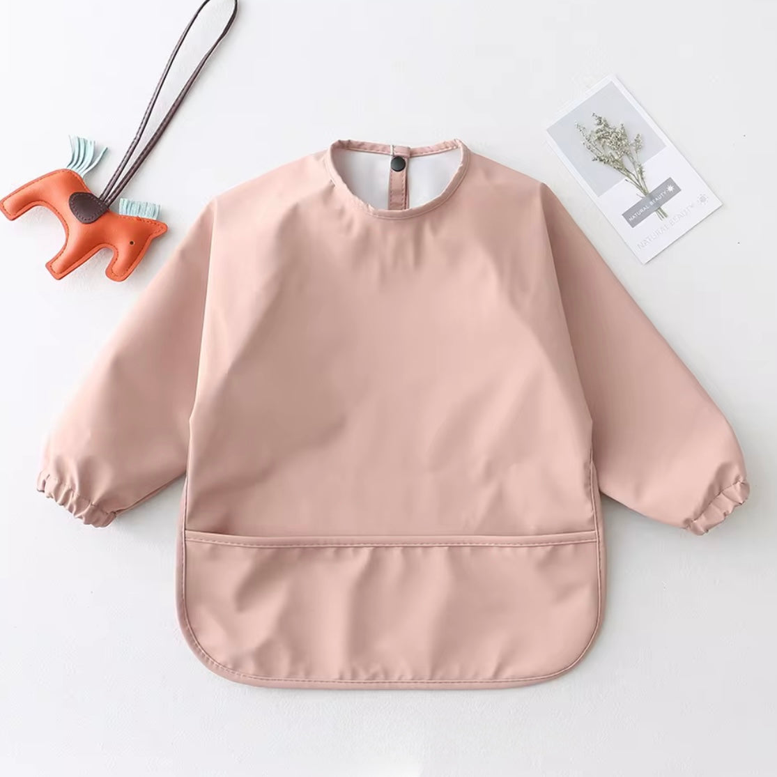 Long-sleeved blush pink smock bib with waterproof material and front pocket.