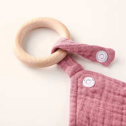 Close-up of natural wooden teething ring attached to soft dusty rose muslin comforter with secure snap closure.