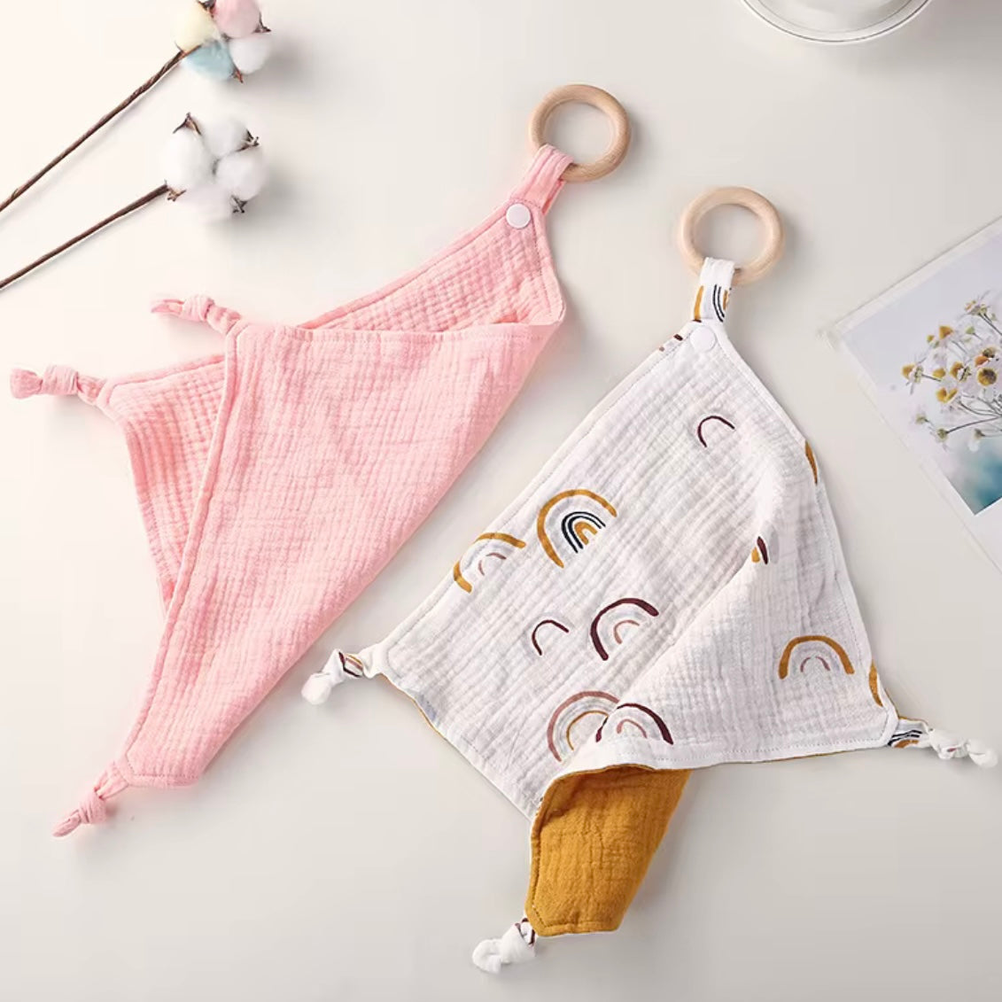 Muslin baby comforters with wooden teethers in blush pink and rainbow print, soft and breathable for newborns and toddlers.