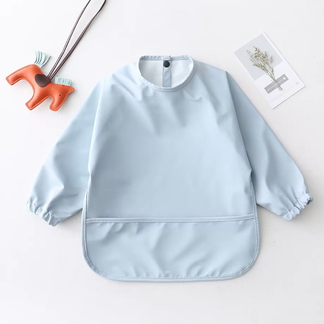 Mess Mate long-sleeved smock bib in pastel blue with waterproof front pocket.
