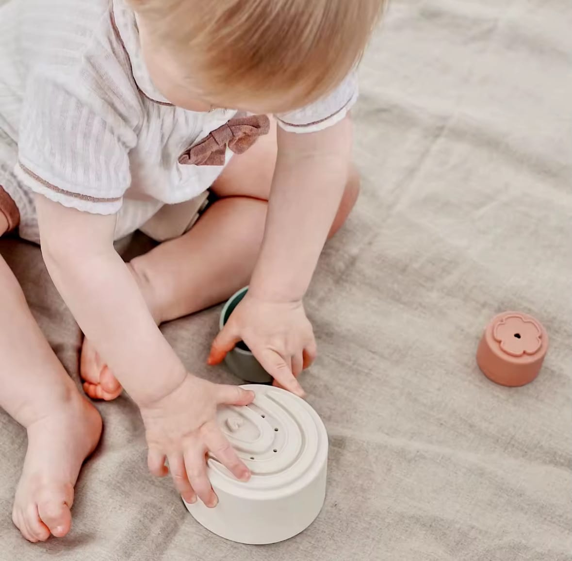 Baby sitting on a play mat using silicone stacking cups. Perfect for sensory play, early learning, and improving hand-eye coordination with safe, soft-touch cups.