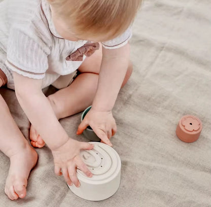 Baby sitting on a play mat using silicone stacking cups. Perfect for sensory play, early learning, and improving hand-eye coordination with safe, soft-touch cups.