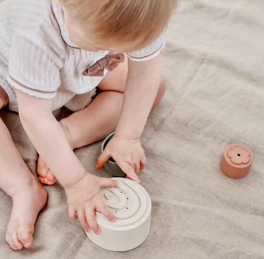 Baby sitting on a play mat using silicone stacking cups. Perfect for sensory play, early learning, and improving hand-eye coordination with safe, soft-touch cups.